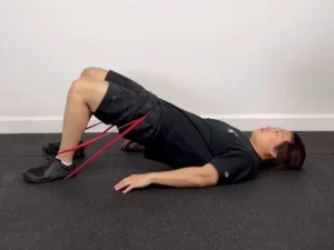 حرکت پل باسن با کش مقاومتی بالای زانو روی مت ورزشی