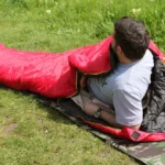 کیسه خواب SnowHawk SPRING 900 رنگ قرمز در محیط کمپینگ روی چمن